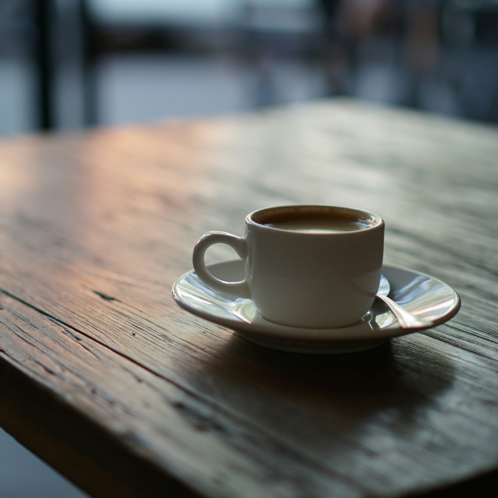 古い木製のテーブルに白いカップのコーヒーがひとつ