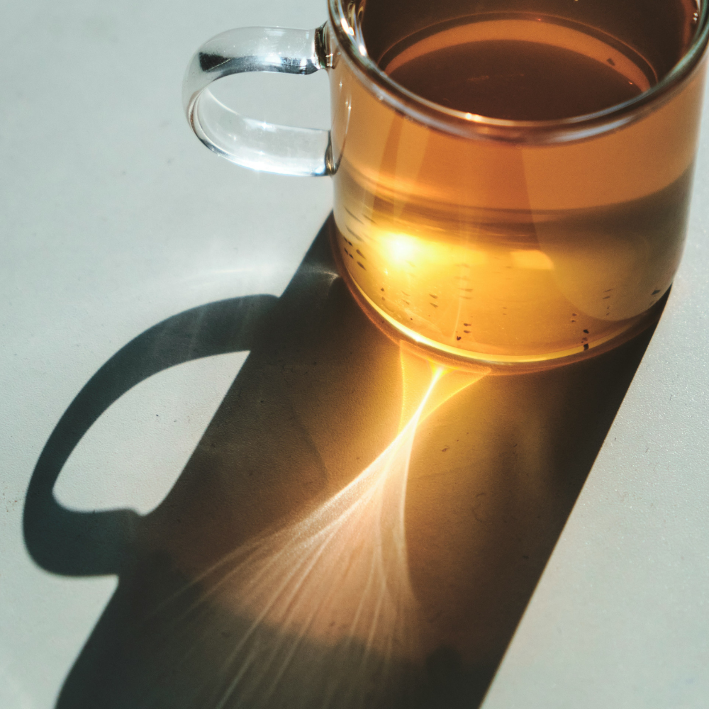 ガラスのマグカップに注がれたお茶。光が差し込み白いテーブルには琥珀色の影が映る