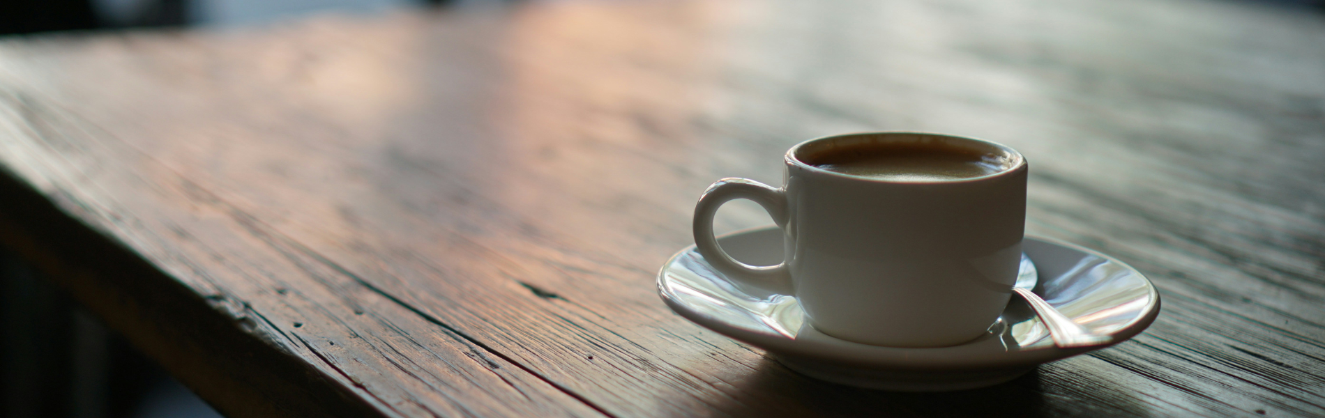 古い木製のテーブルに白いカップのコーヒーがひとつ